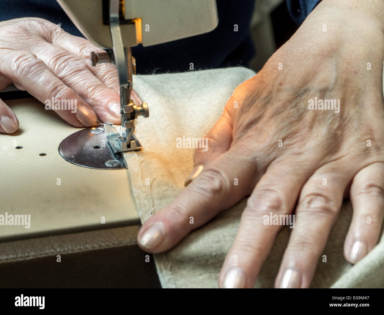 Closeup of senior woman's hands sawing linen border with sewing machine Stock Photo