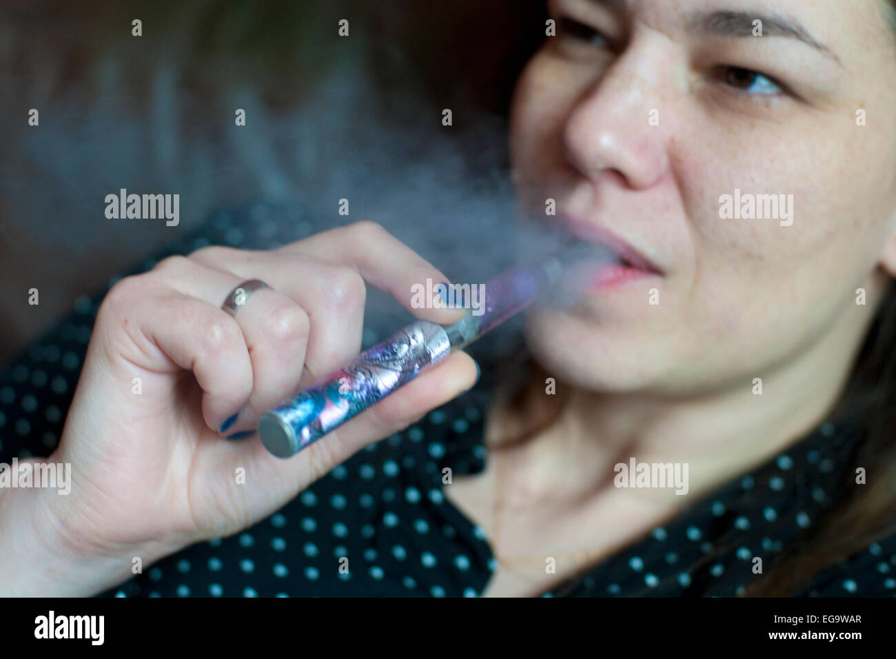 a woman relaxing smoking an e cigarette and blowing out vapour Stock Photo