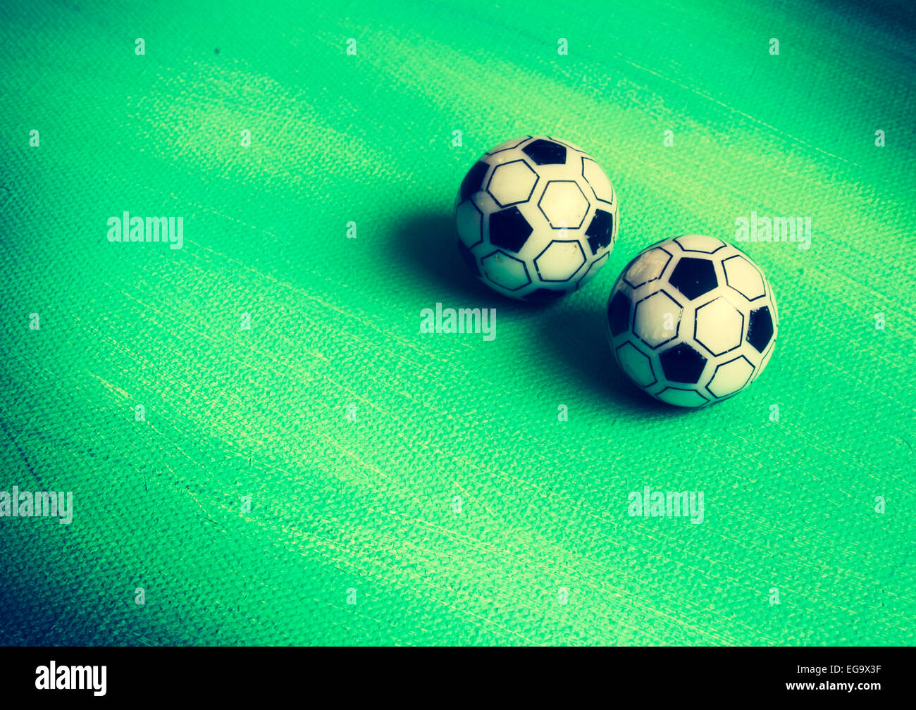Two soccer toy balls on green canvas for grass, playful background. Stock Photo