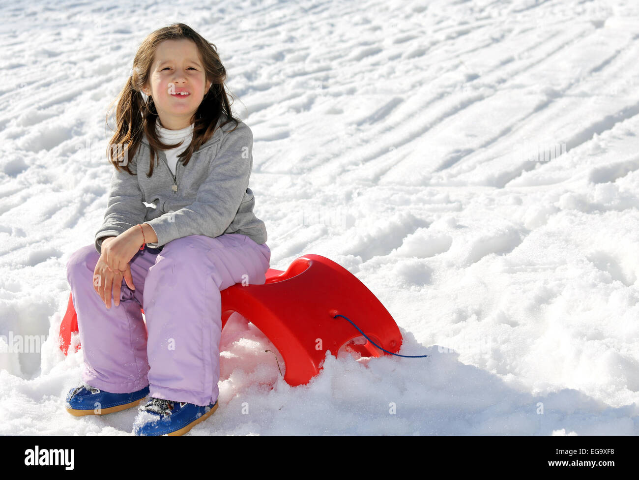 pretty girl plays with the Red sled on the snow in the winter in the mountains Stock Photo