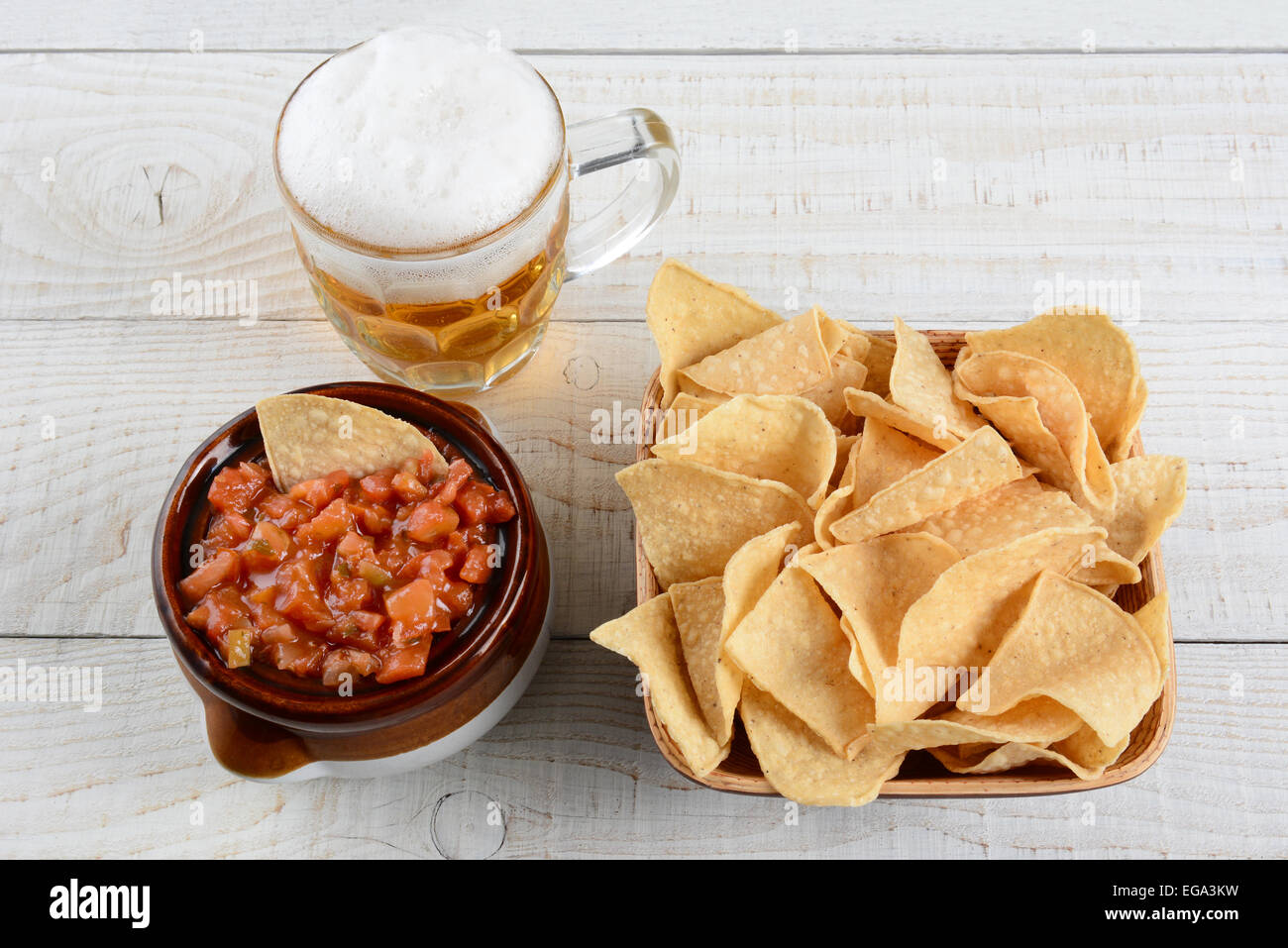 High angle shot of a bowl of corn chips a crock full of fresh salsa and mug of beer on a whitewashed rustic wood table. Stock Photo