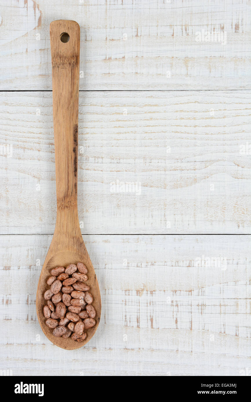 HIgh angle shot of a wooden spoon full of uncooked pinto beans. Vertical format on a rustic white wood kitchen table. Stock Photo