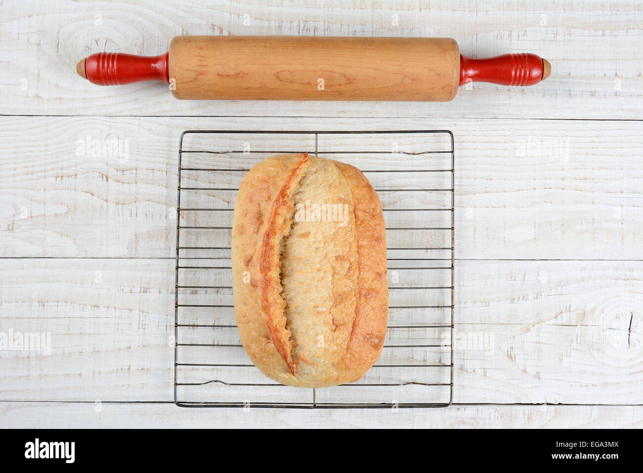 High angle shot of a rolling pin and a fresh baked loaf of bread on a cooling rack. Horizontal format on a rustic whitewashed ki Stock Photo