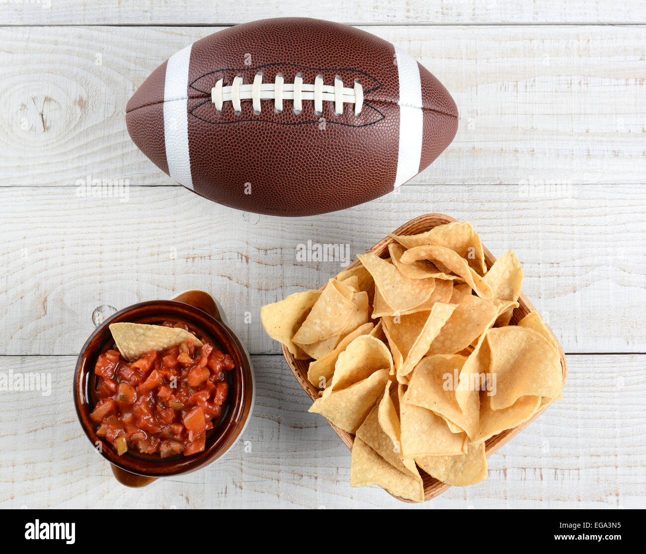 High angle shot of a bowl of corn chips a crock full of fresh salsa and an American football on a whitewashed rustic wood table. Stock Photo