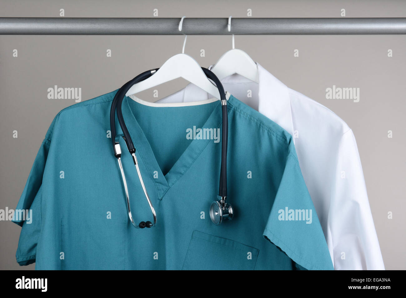 Closeup of a doctor's scrubs with stethoscope and lab coat on hangers against a neutral background. Green Scrubs and a white lab Stock Photo