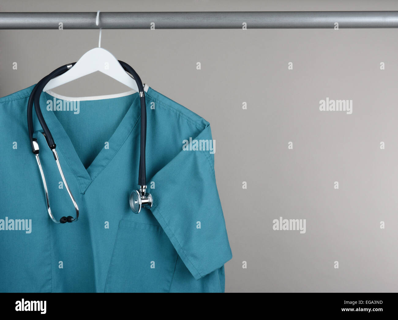 Closeup of a doctor's scrubs and stethoscope on hanger against a neutral background. Green surgical smock on a white hanger with Stock Photo