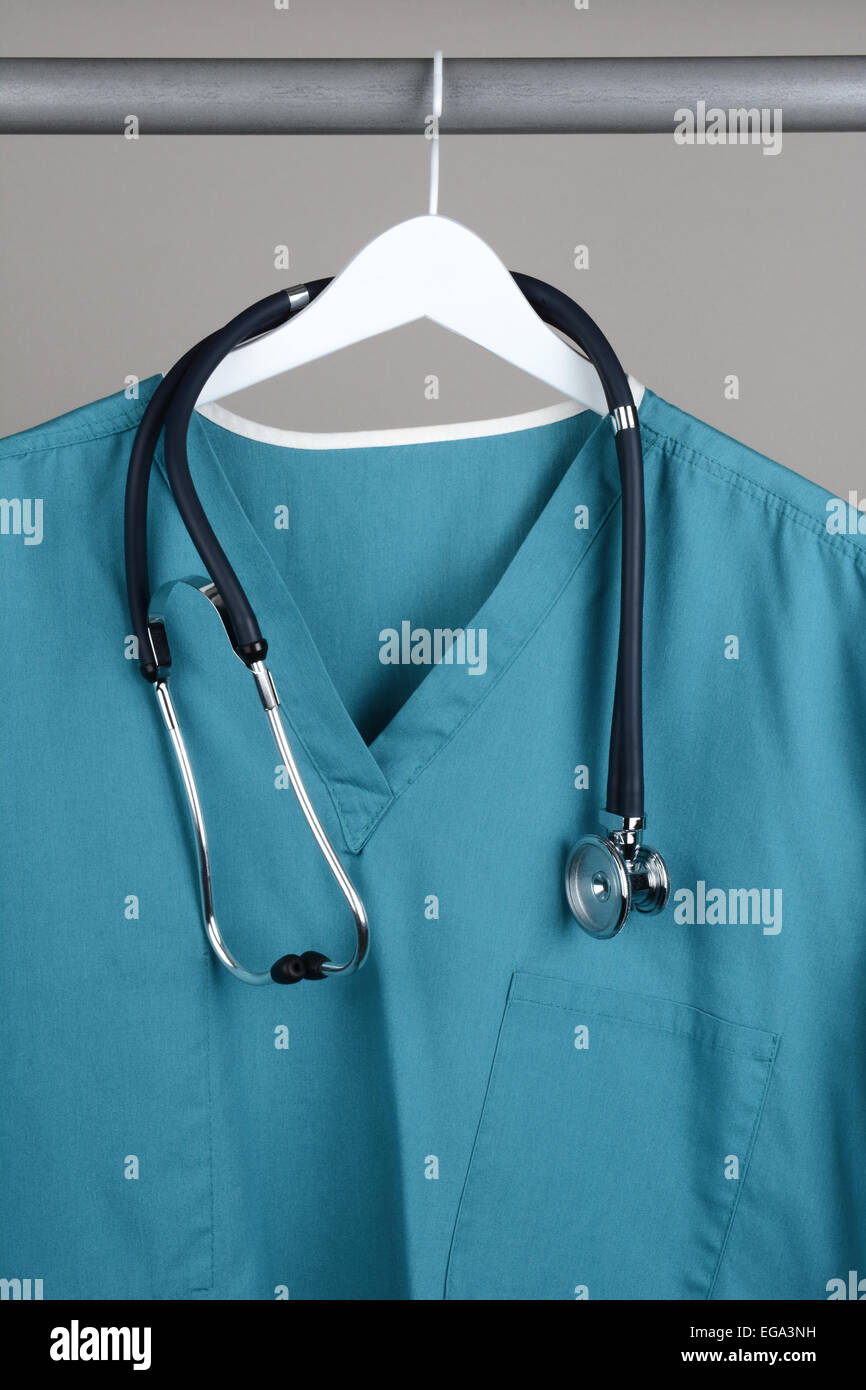 A surgeon's scrubs and stethoscope on hanger against a gray background. Closeup on a white hanger with a gray background in vert Stock Photo
