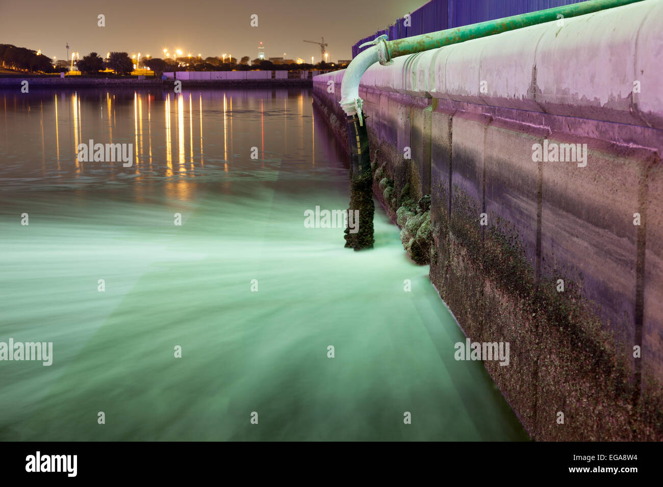 Sewage pipe discharging water into a river at night. Dubai Creek, UAE Stock Photo