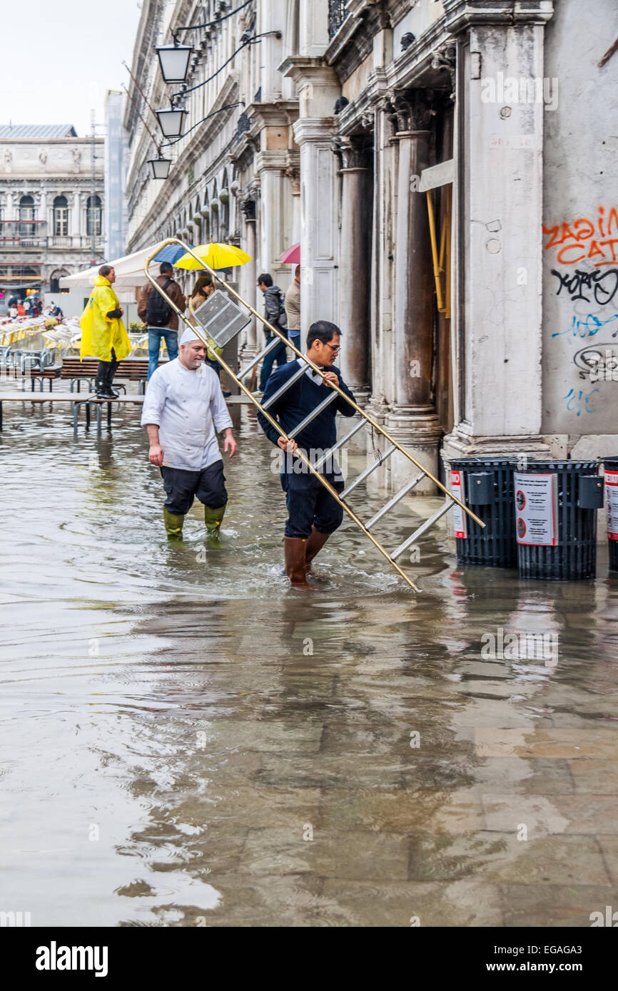 Workmen going about their business during flooding (acqua alta) in St Marks Square, Venice Italy Stock Photo