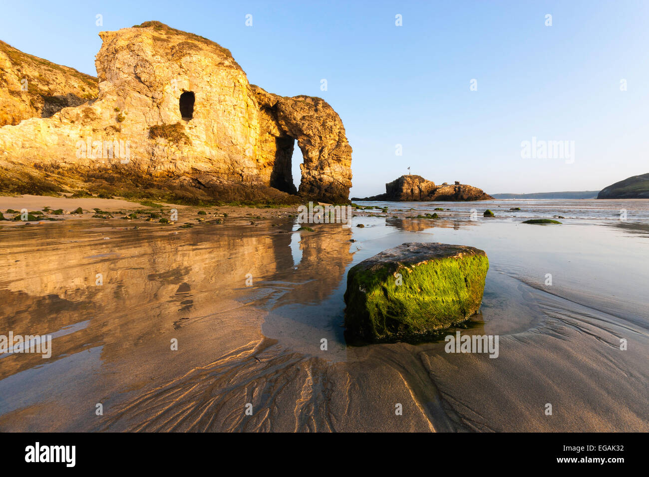 Perranporth beach at sunrise on a clear morning showing a large arch in the headland reflecting in the water on the sand. Stock Photo