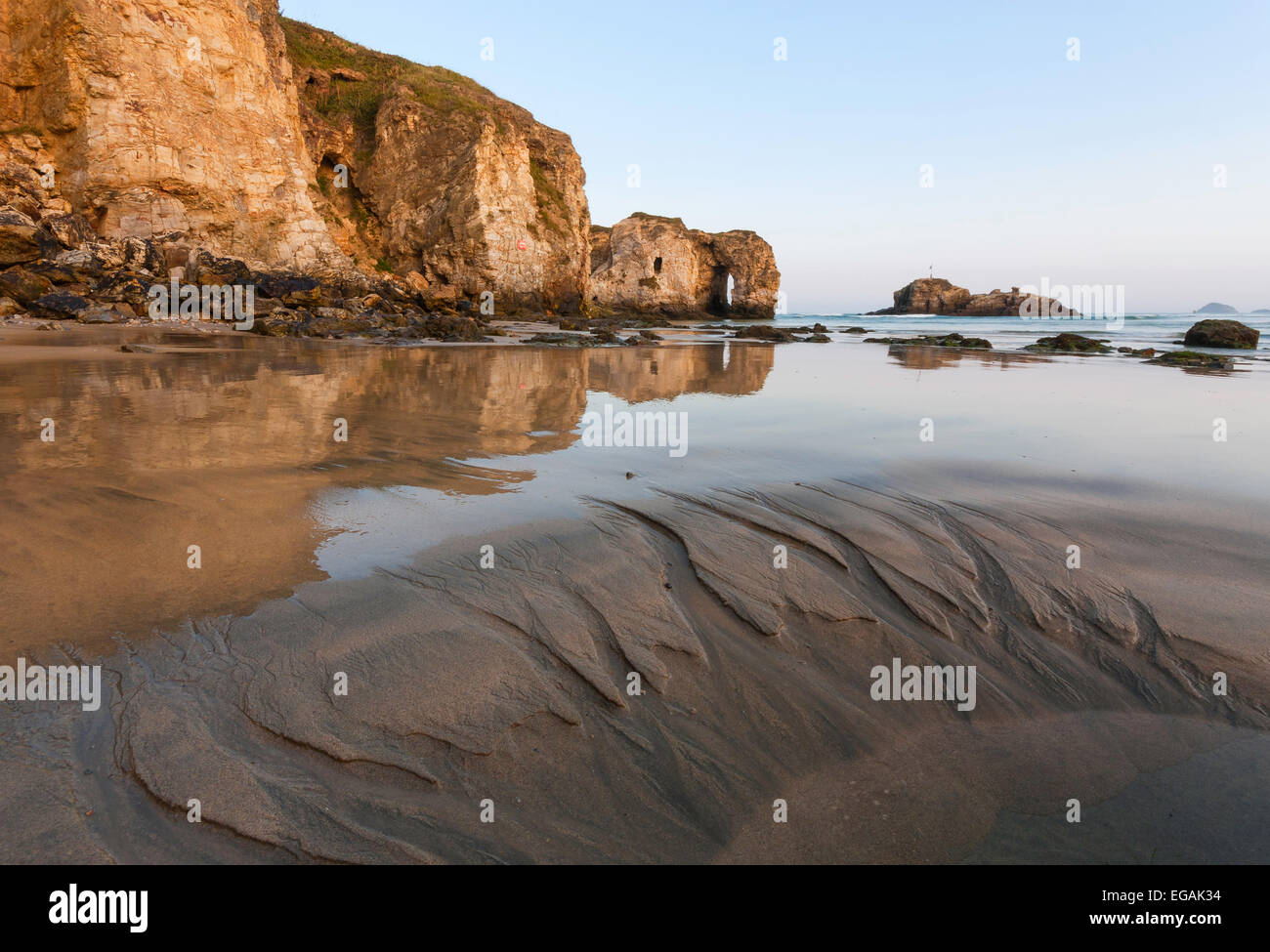 Perranporth's impressive natural arch reflects on the sandy beach on a clear morning. There are patterns in the sand. Stock Photo