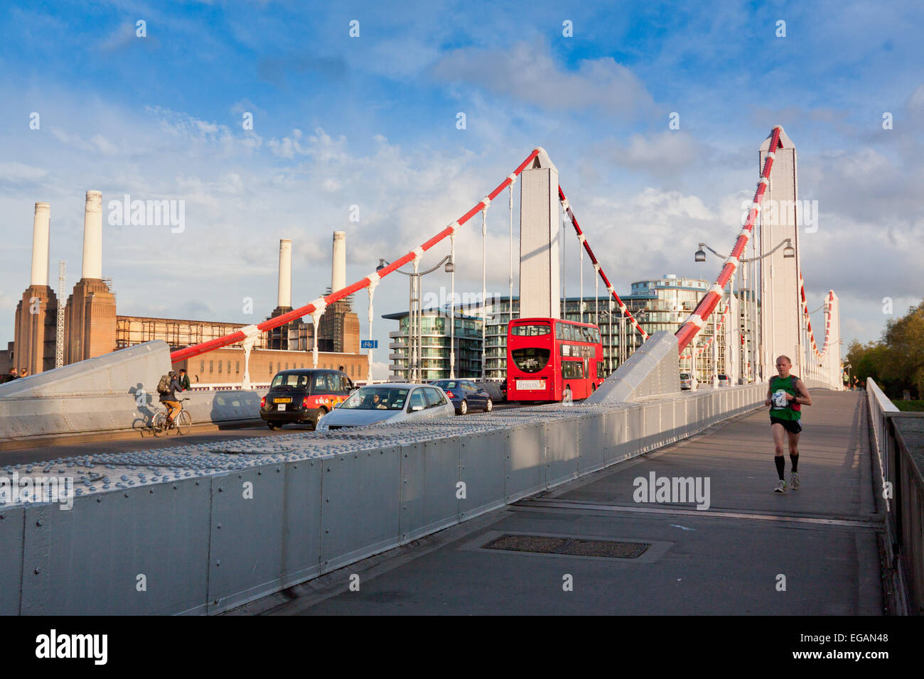 Man running across Chelsea Bridge with traffic and Battersea Power Station behind, London, England Stock Photo