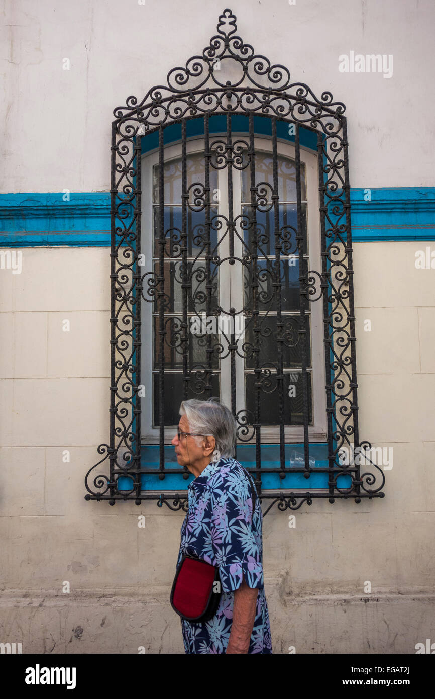 old woman walking past a window of old house with decorative iron grille, Calle San Isidro, Santiago, Chile Stock Photo