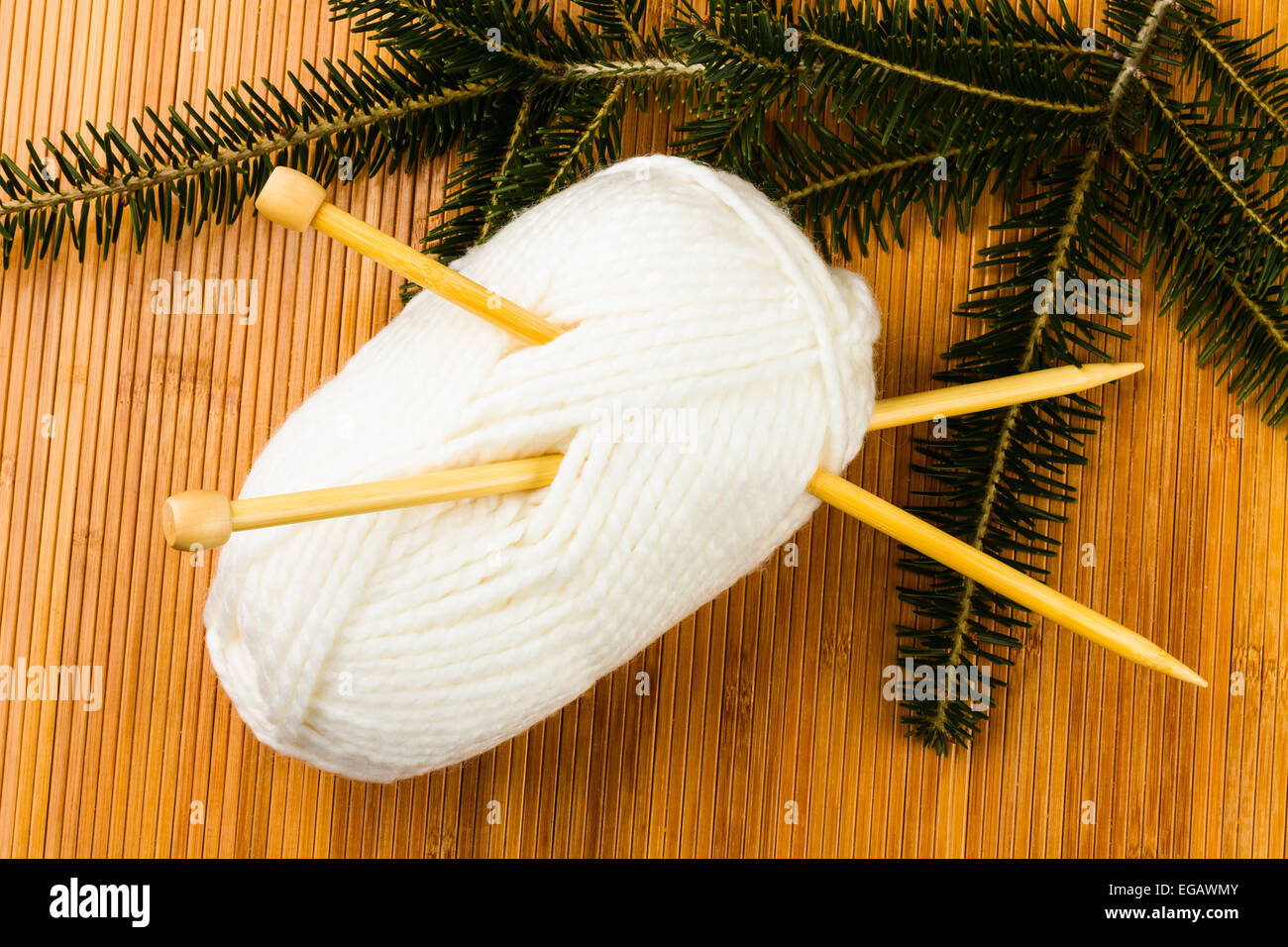 roll of white soft knitting yarn and yew branch on wooden background Stock Photo