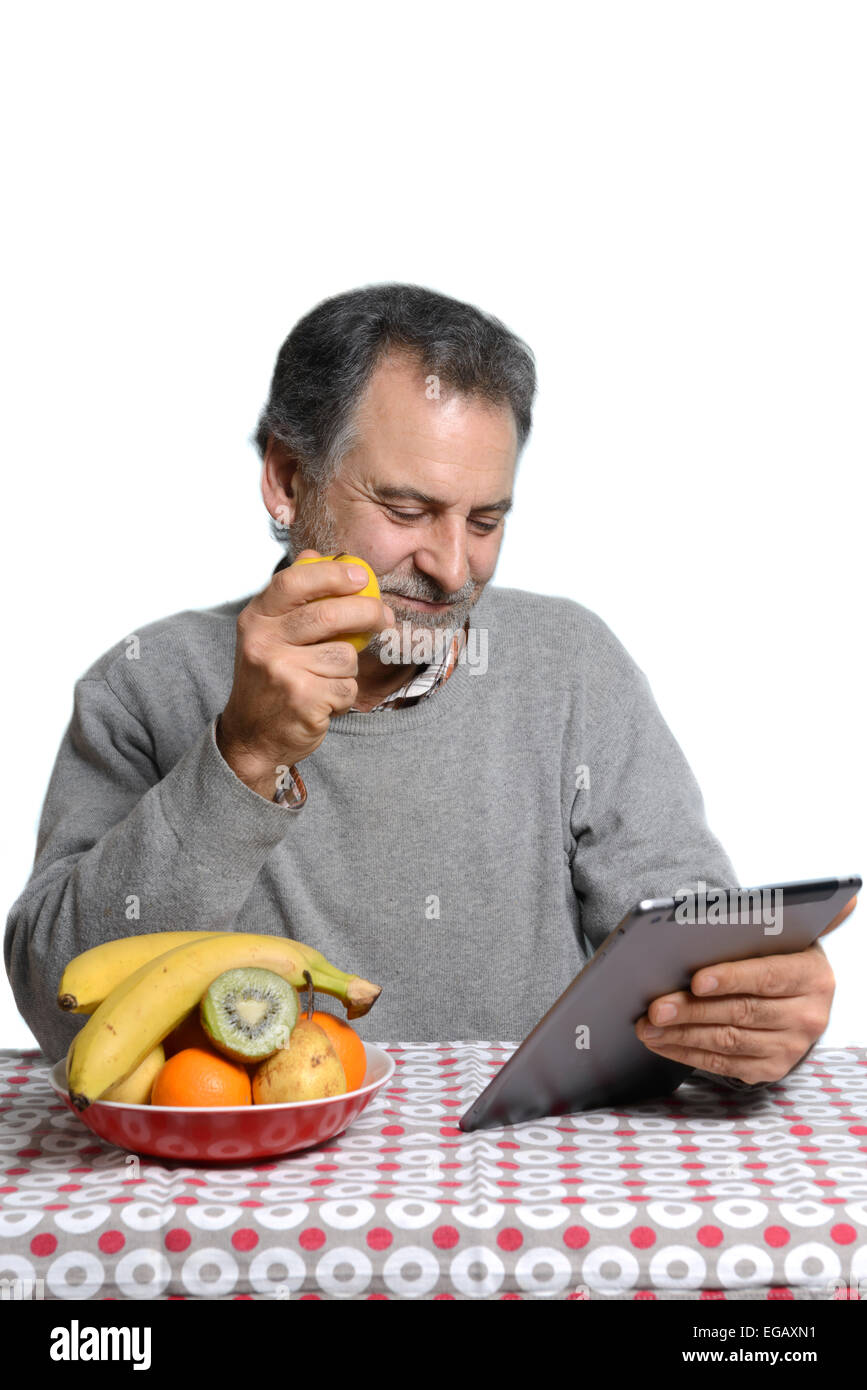 Middle aged man using a tablet computer while eating fruit at home Stock Photo