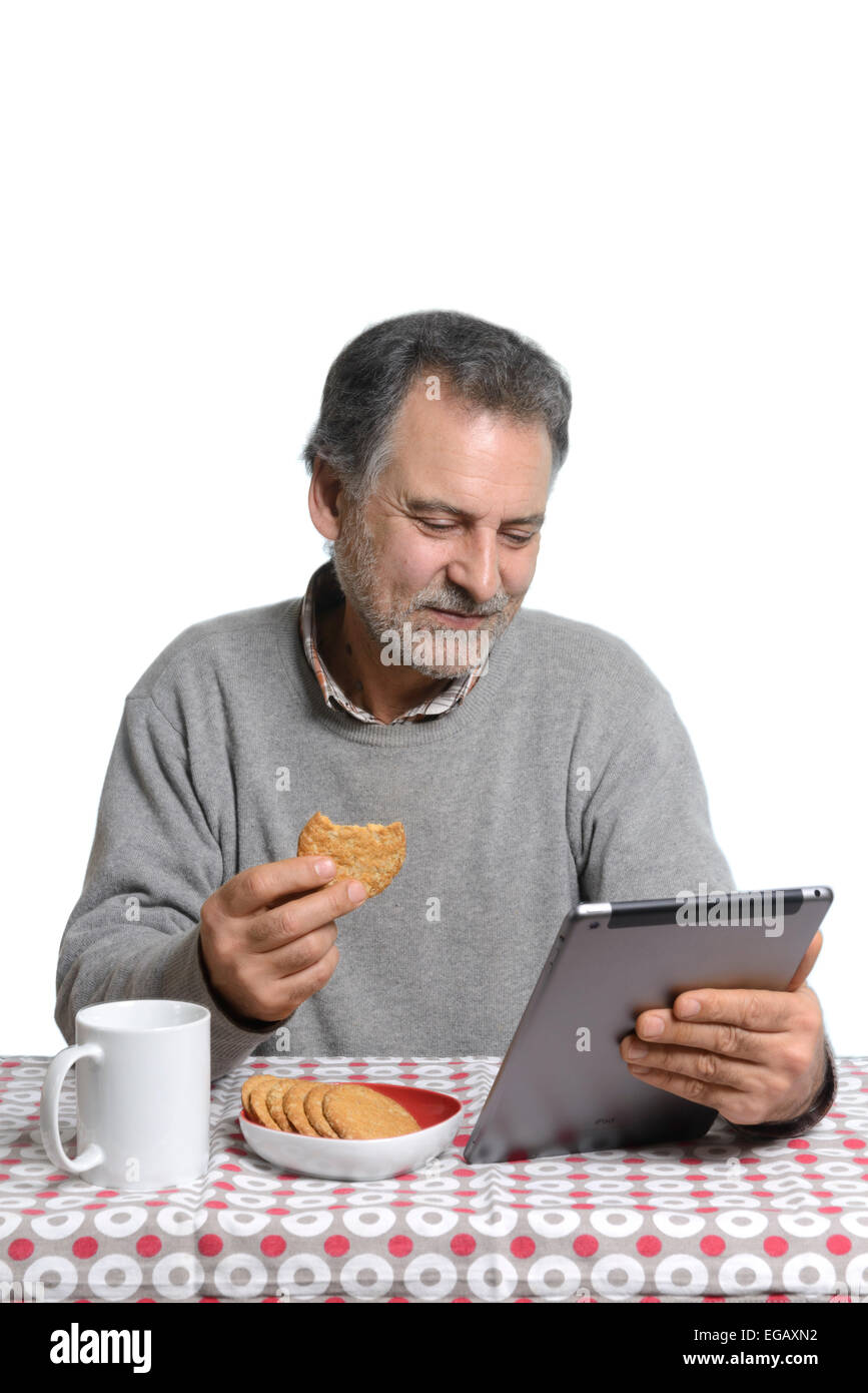 Middle aged man using a tablet computer while eating milk and cookies at home Stock Photo