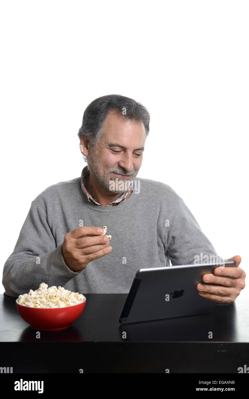 Middle aged man using an Apple iPad Air tablet while eating popcorn at home Stock Photo