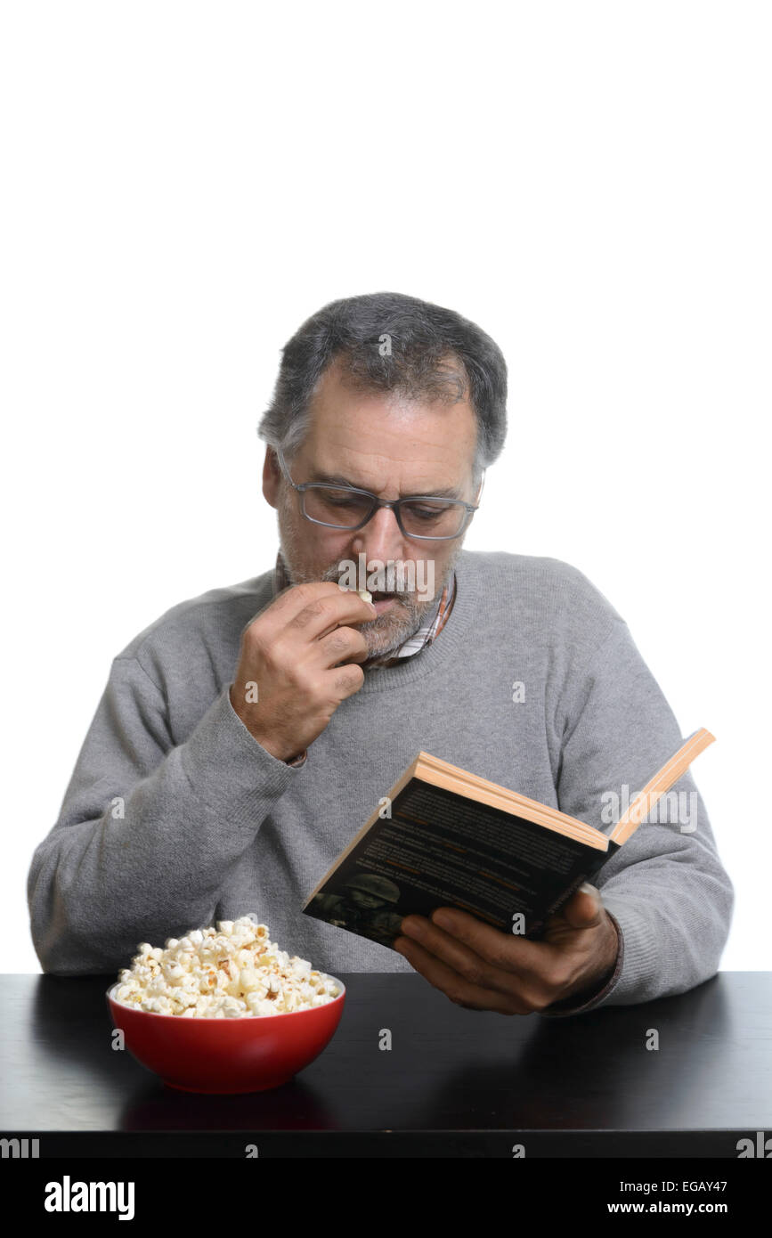Middle aged man reading a book while eating popcorn at home Stock Photo