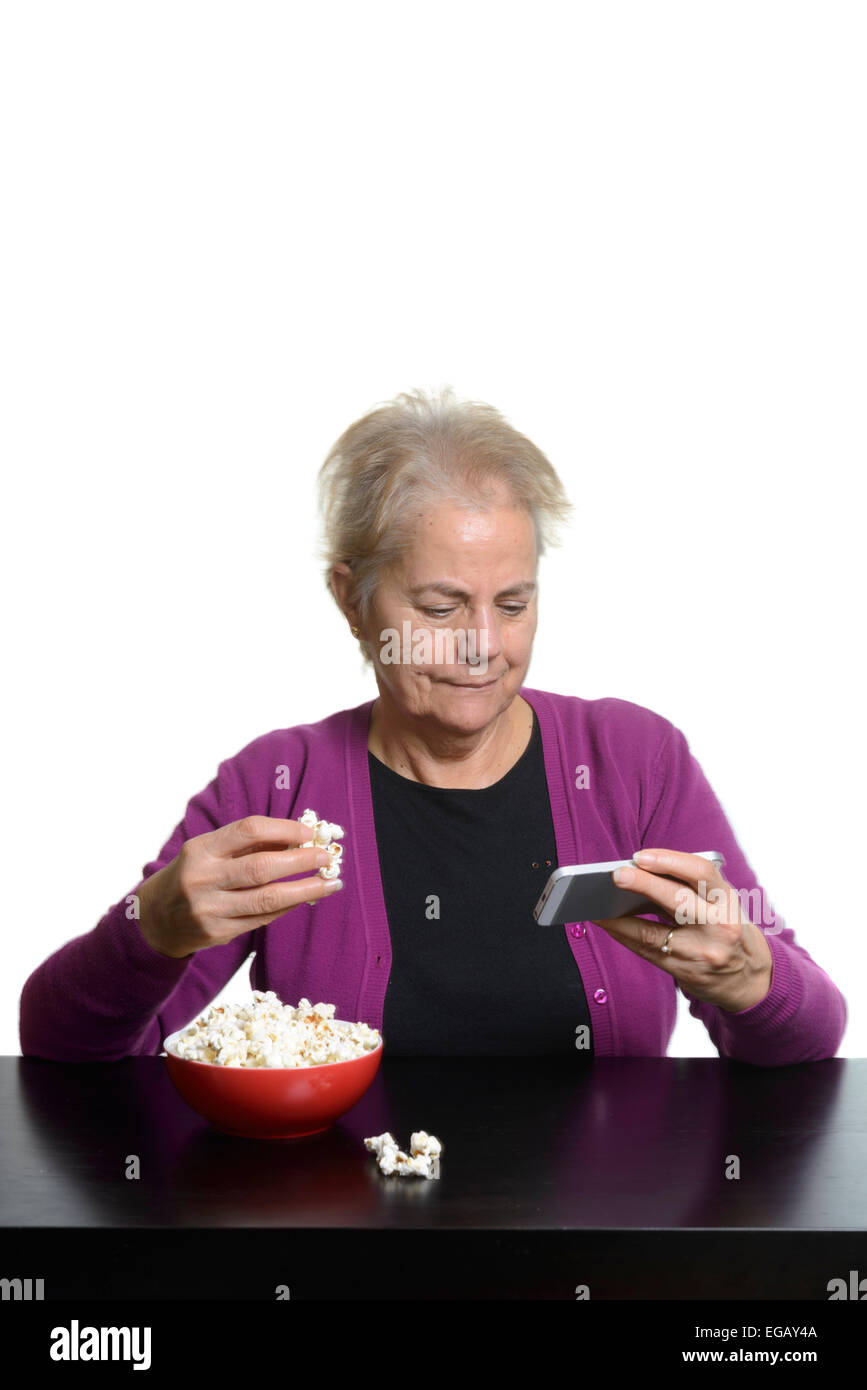 Middle aged woman eating popcorn while watching a movie on an Apple iPhone smart phone Stock Photo