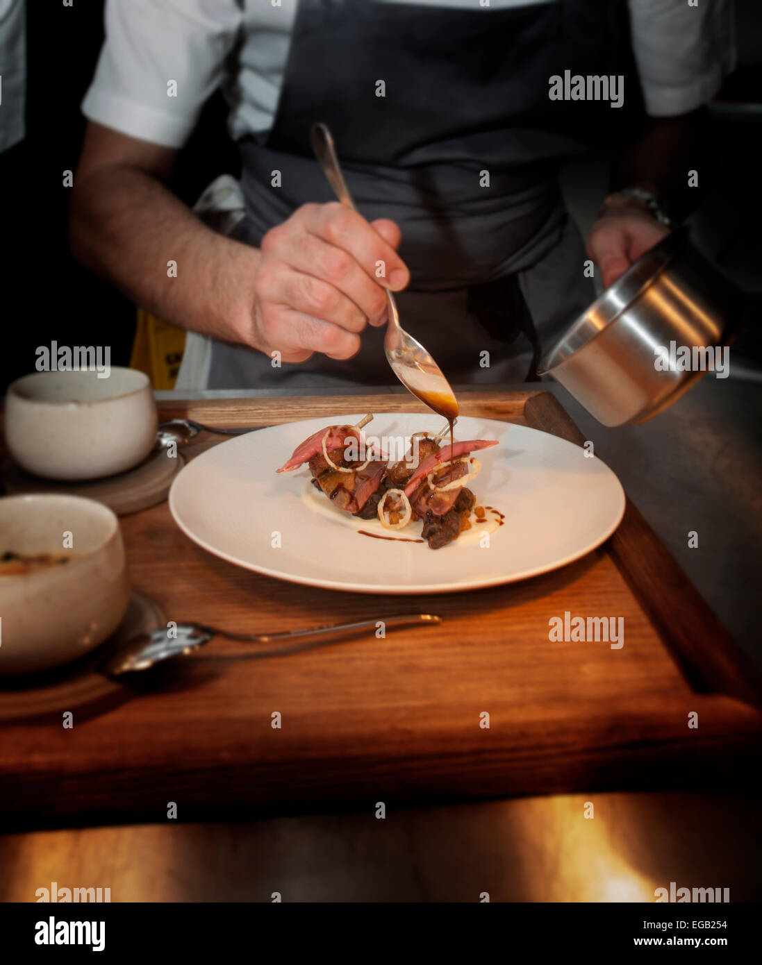 Chef working in the kitchen finishes preparing dish by adding sauce at Sixty One Restaurant London Stock Photo