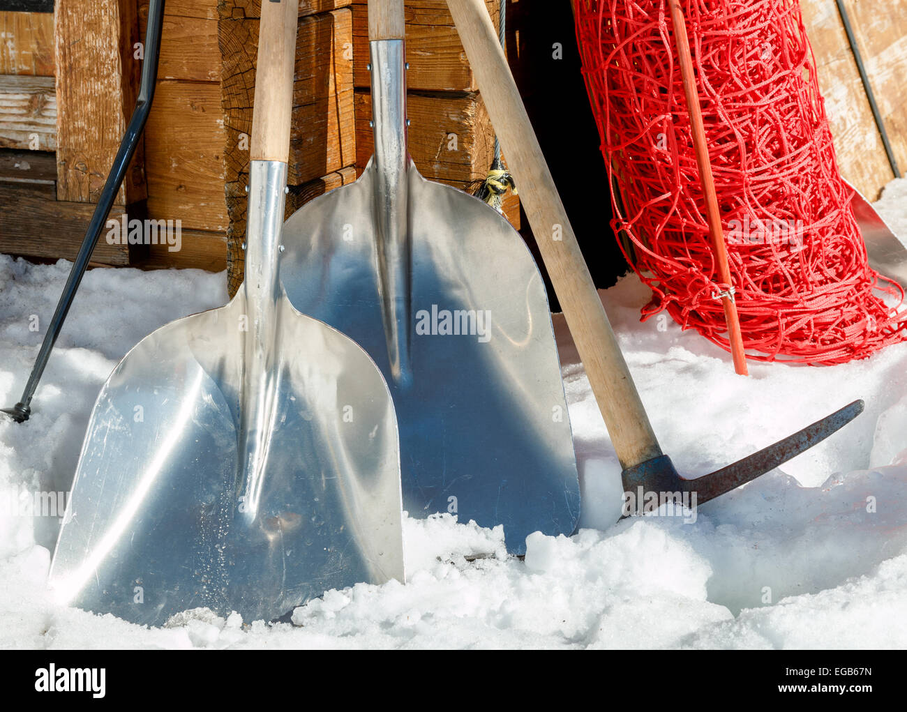 Snow shovels, pick axe and other snow clearance  equipment leaning against a shed . Stock Photo
