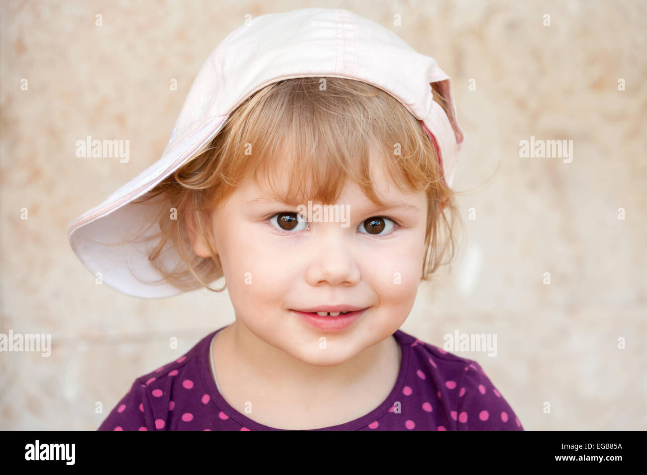 Outdoor closeup portrait of smiling cute Caucasian blond baby girl in white baseball cap Stock Photo