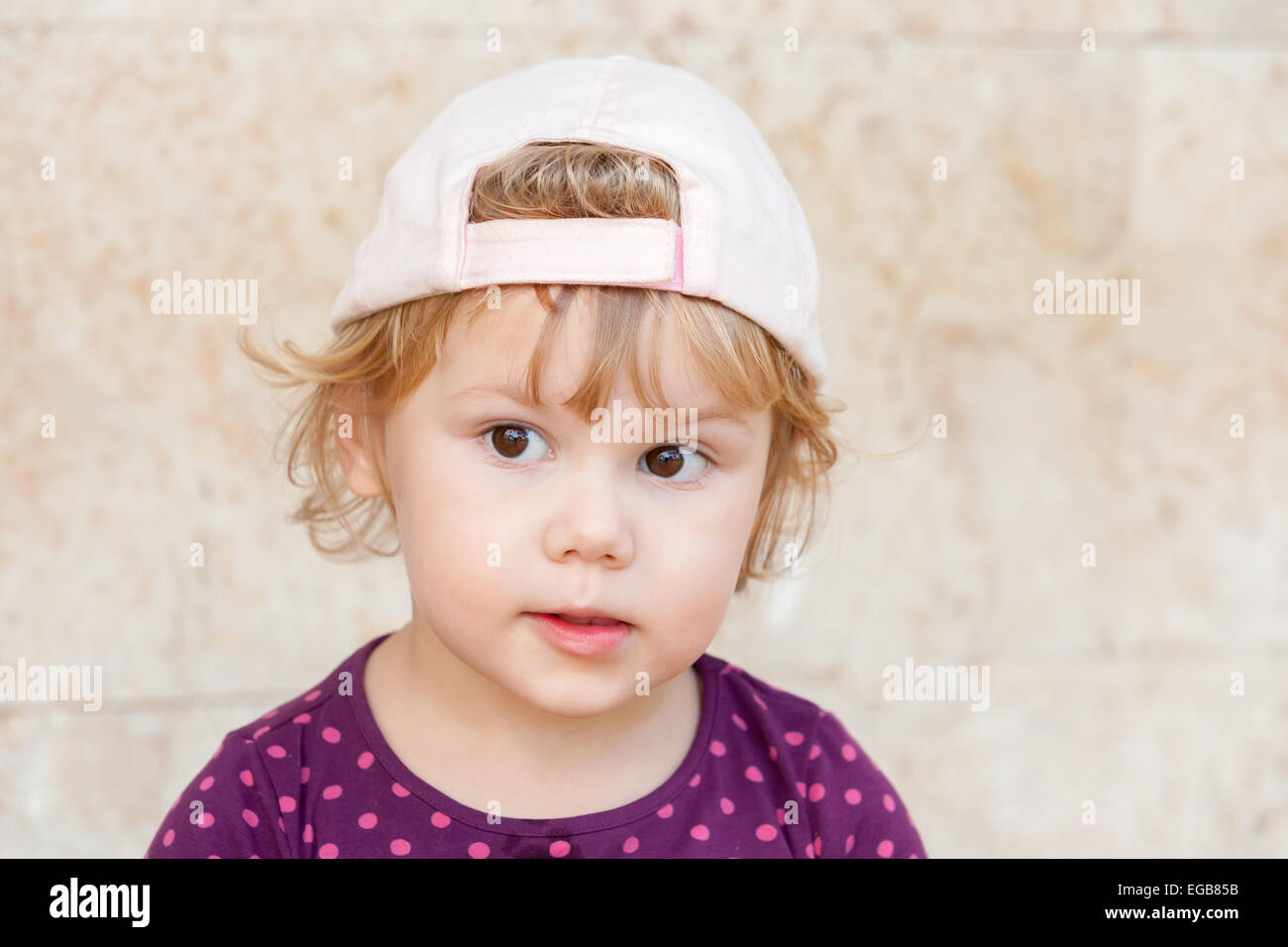 Outdoor closeup portrait of curious cute Caucasian blond baby girl in white baseball cap Stock Photo