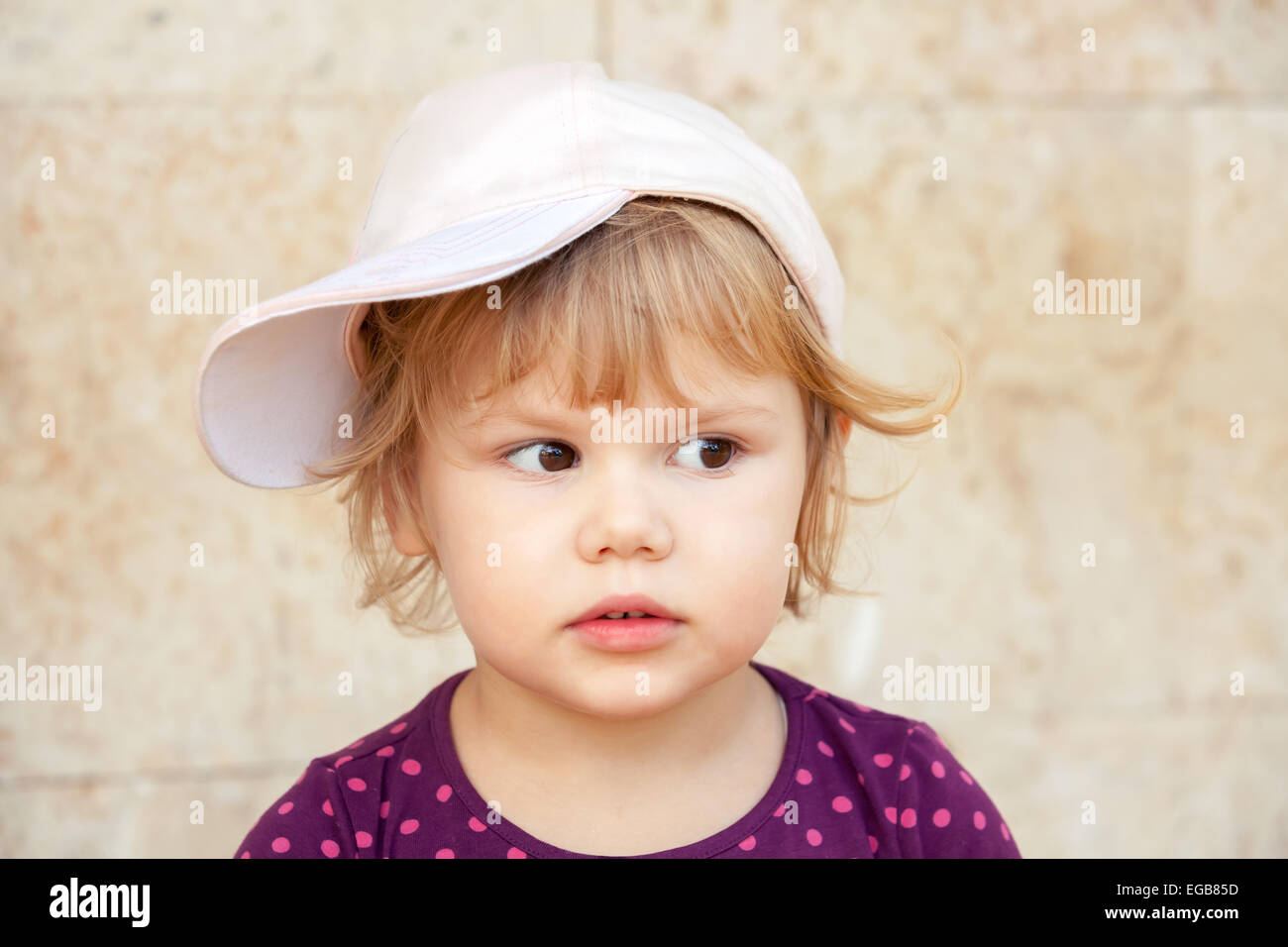 Outdoor closeup portrait of curious cute Caucasian blond baby girl in baseball cap Stock Photo