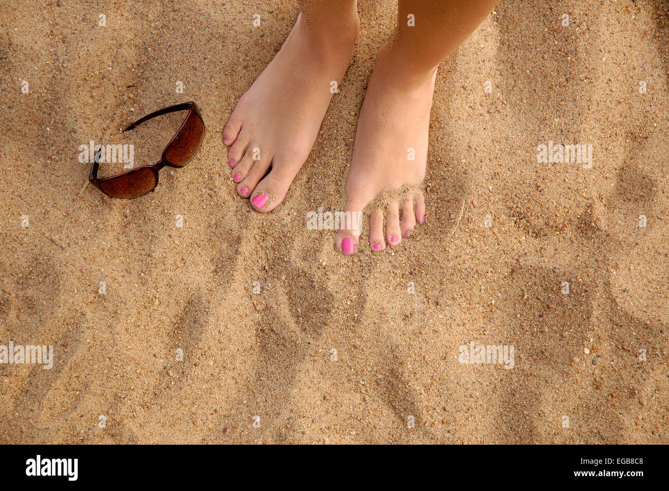 A woman's feet in the sand, standing on a beach. Her toenails are ...