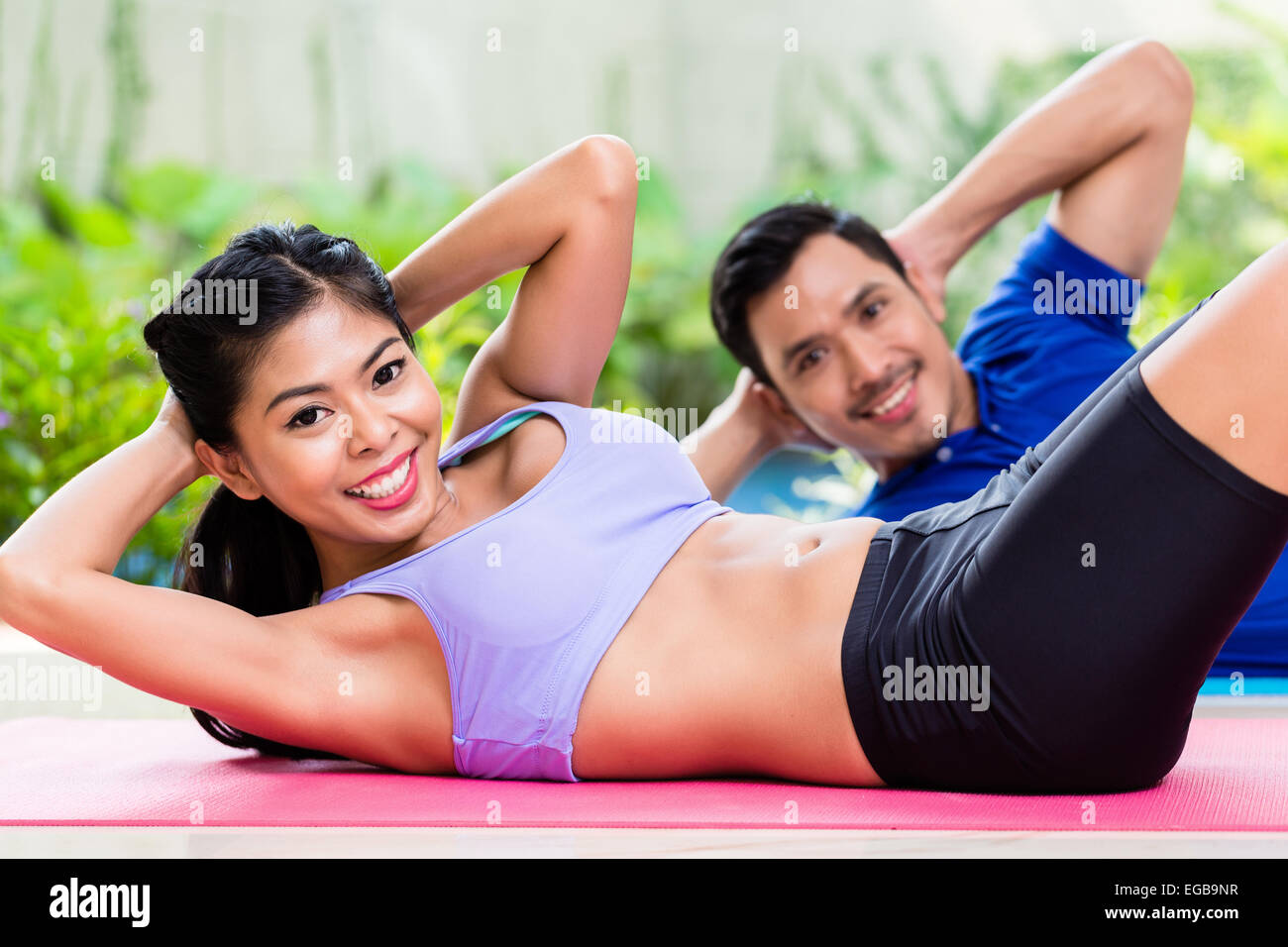 Asian fitness couple, man and woman, doing sit-up in tropical home Stock Photo