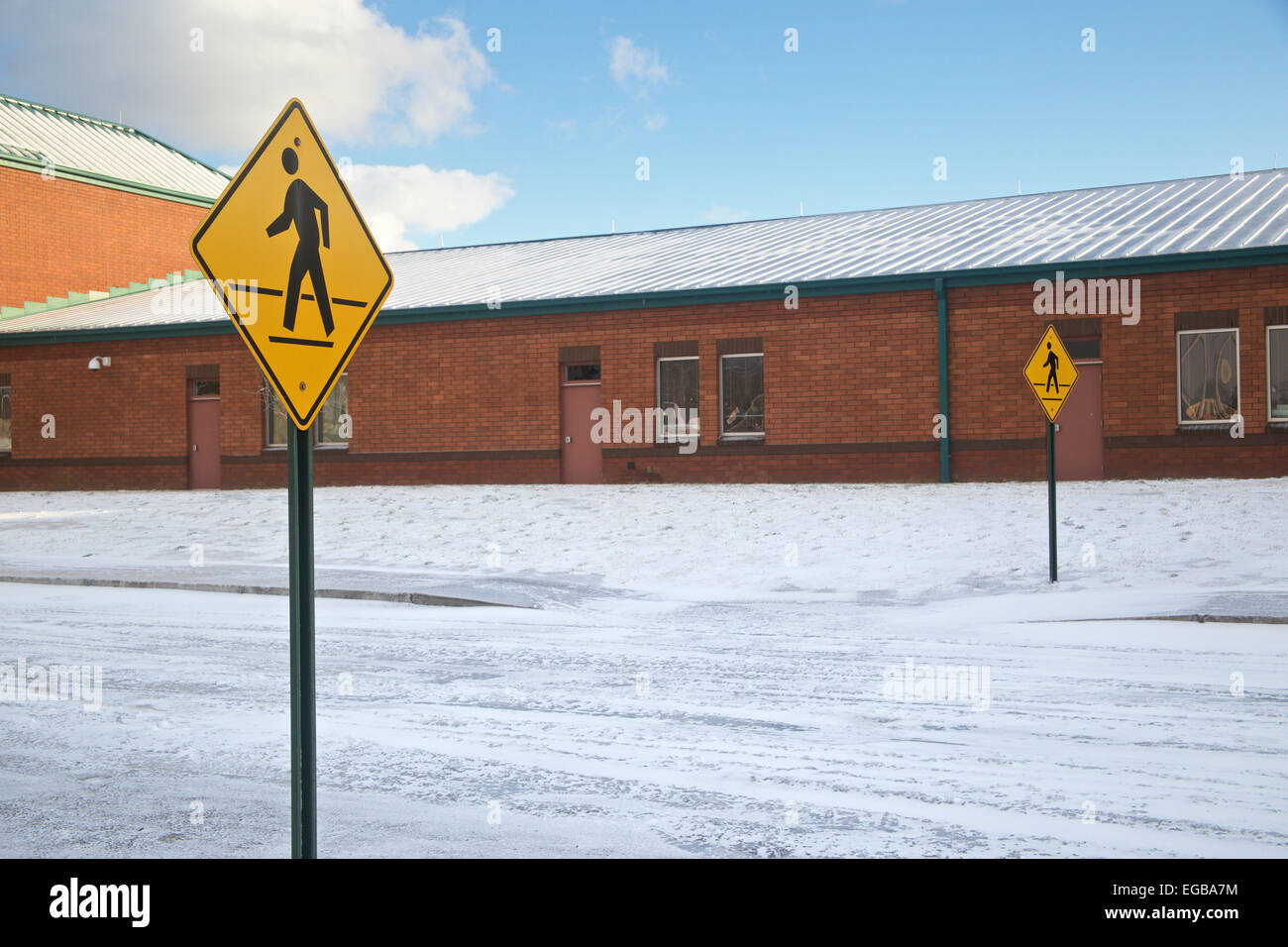 Two Pedestrian crossing signs in front of snow covered elementary school building. Stock Photo