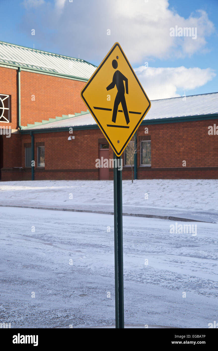 Pedestrian crossing sign in front of snow covered elementary school building. Stock Photo
