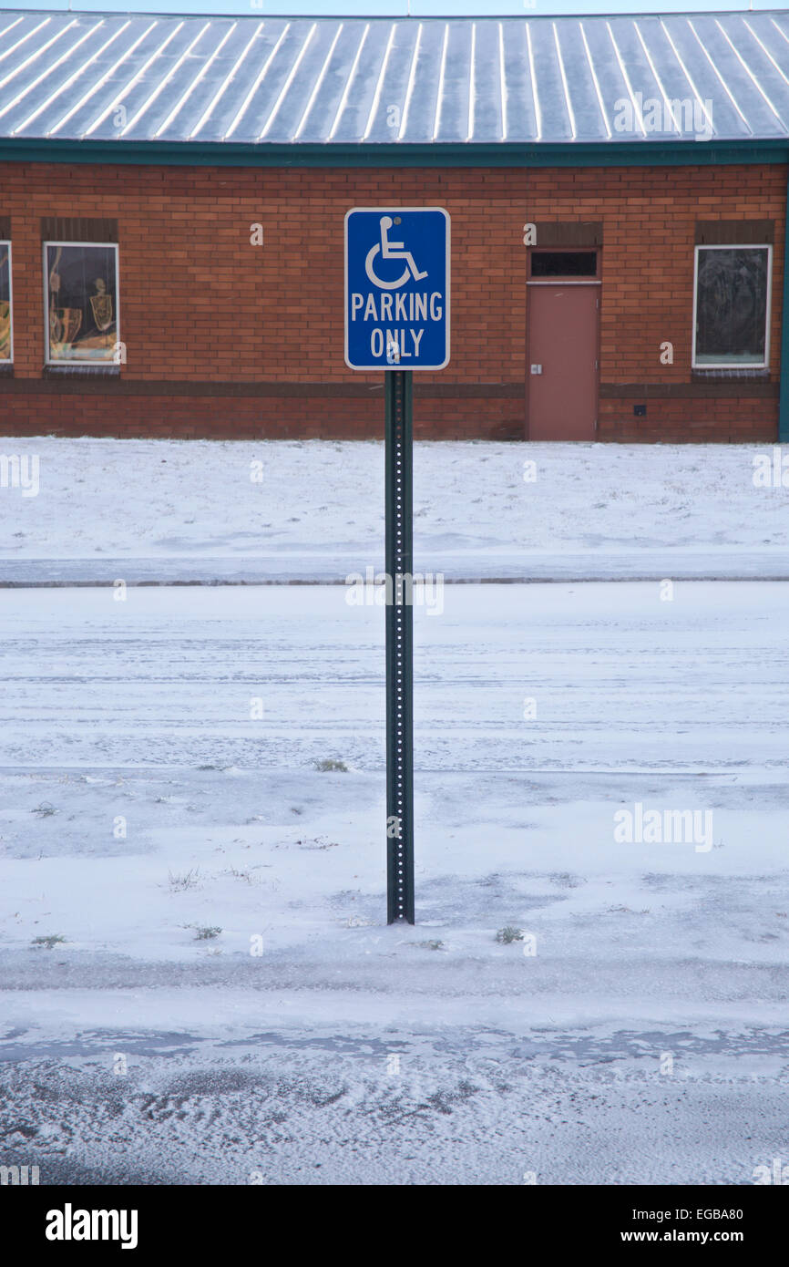 Handicapped parking only sign in snow parking lot in front of an elementary school. Stock Photo