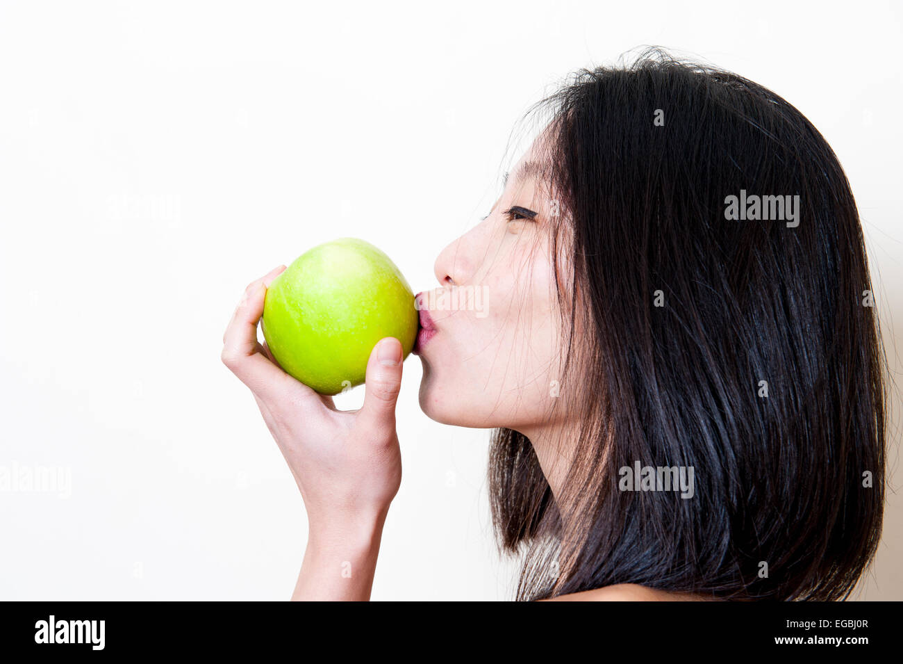 Young beautiful asian woman kissing green apple profile portrait on white background Stock Photo