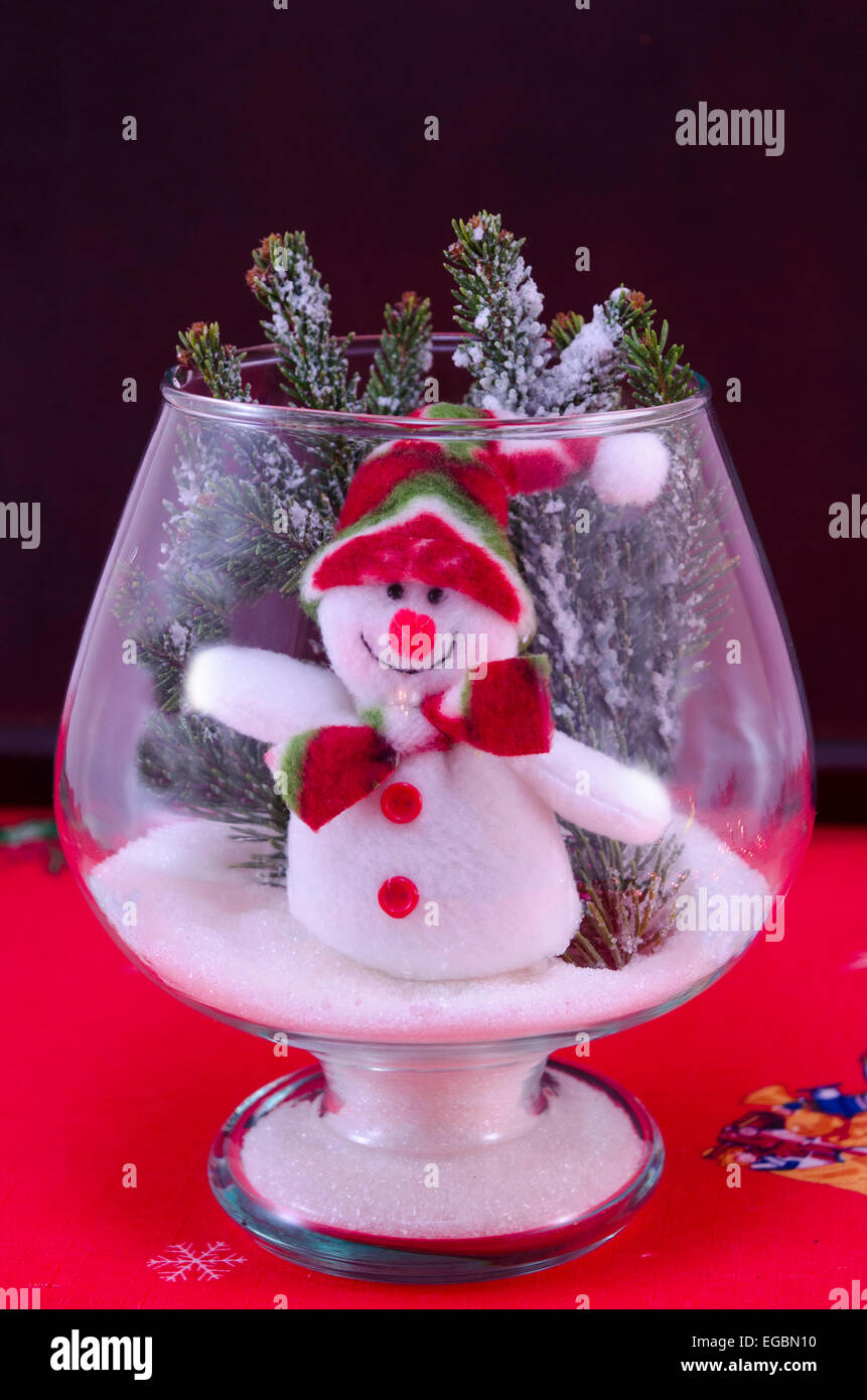 Toy snowman in a glass vase decorated with fir branches on a red tablecloth Stock Photo