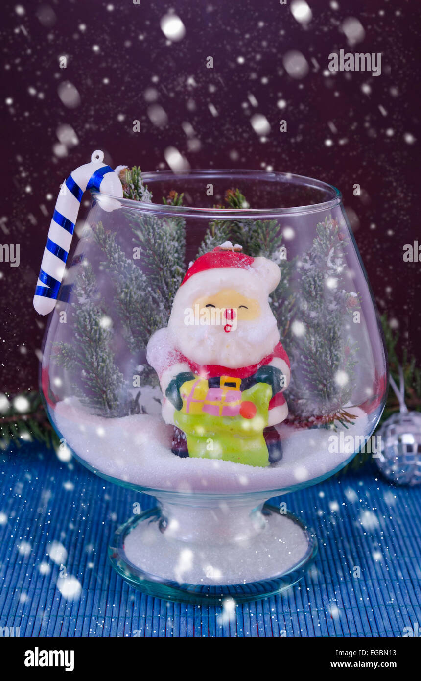 Snowing over Santa shaped candle in a glass vase, against a blue background Stock Photo