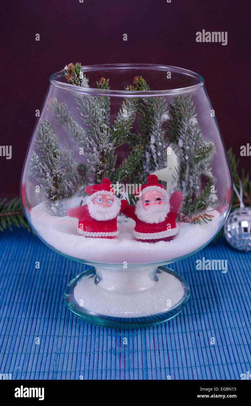 Two toy Santas in a glass bowl covered with snow against a blue background Stock Photo