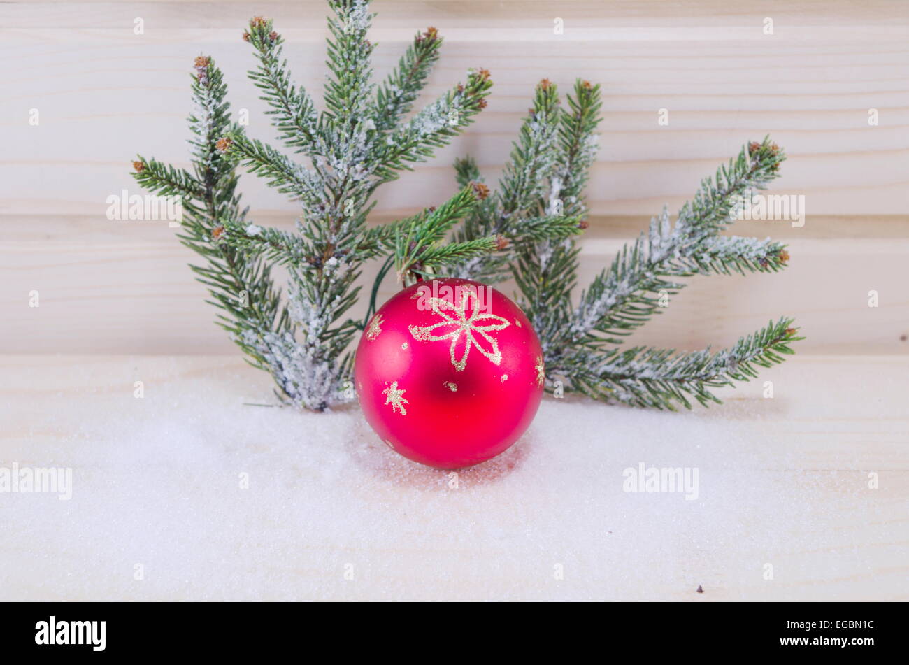 Red Christmas ornament and a fir tree covered with snow, on a wooden surface Stock Photo