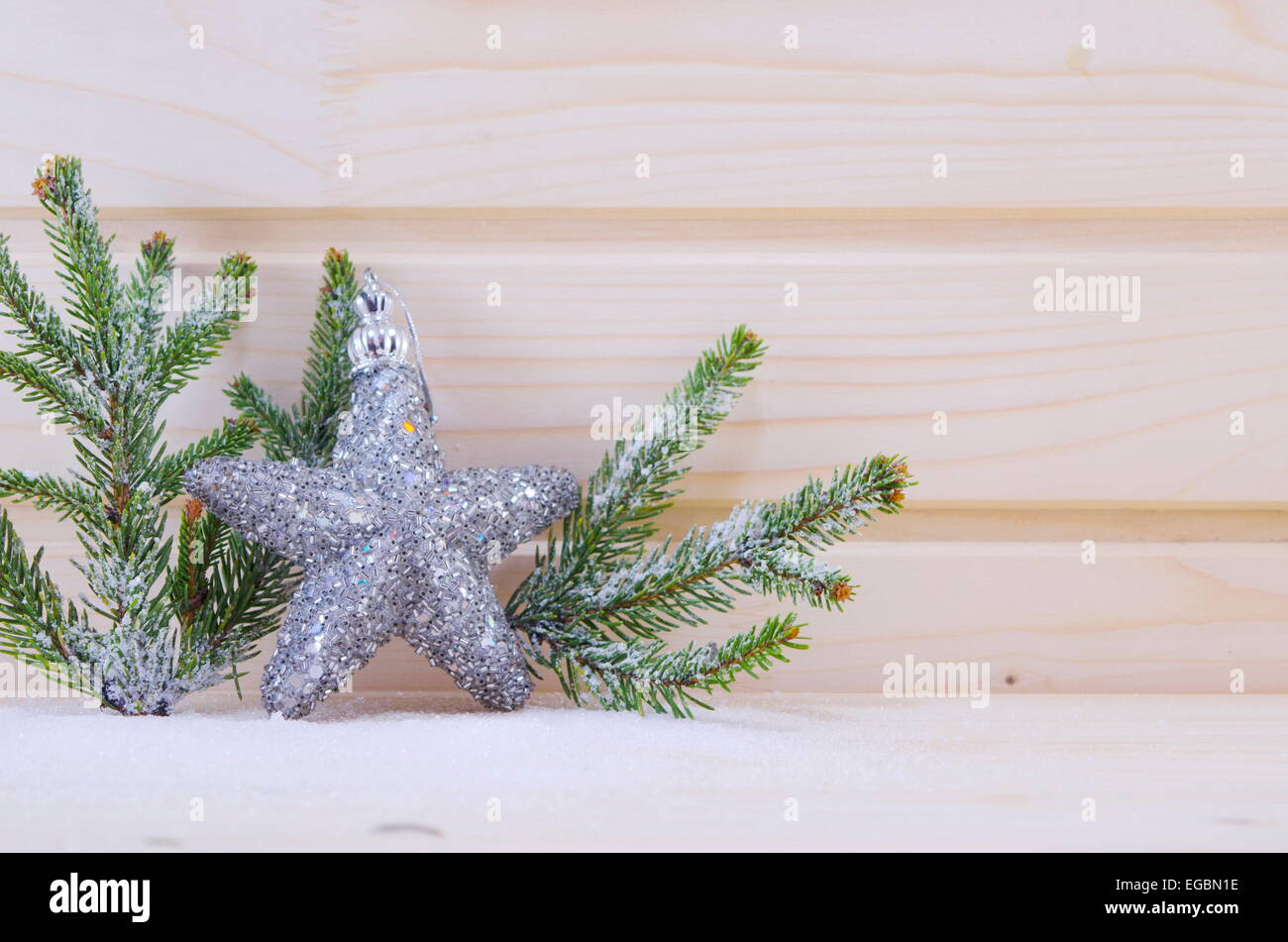 A shiny star ornament with fir branches on a wooden surface covered with snow Stock Photo