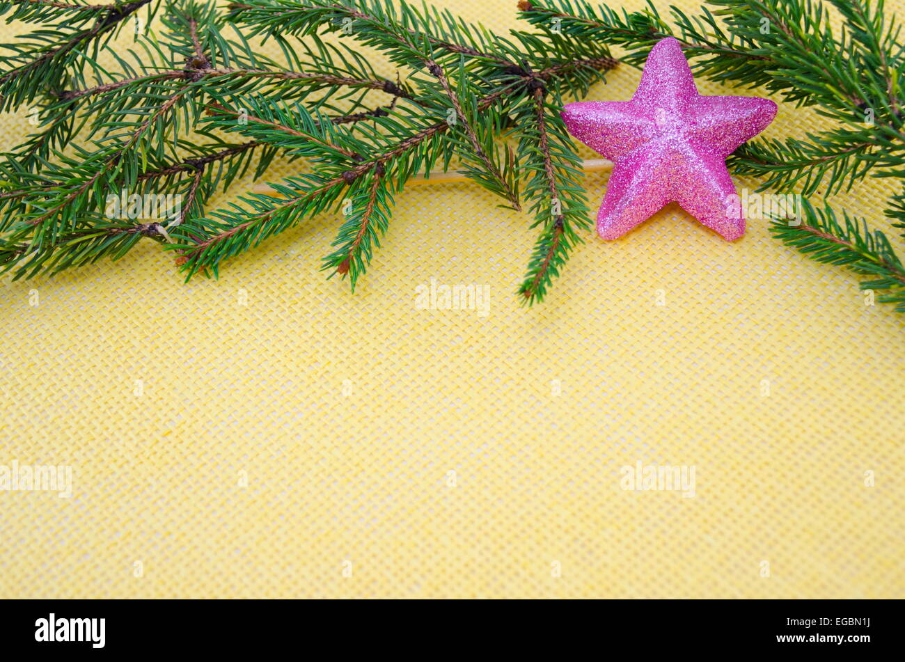 Pink and shiny star ornament with fir branches on a yellow table cloth Stock Photo