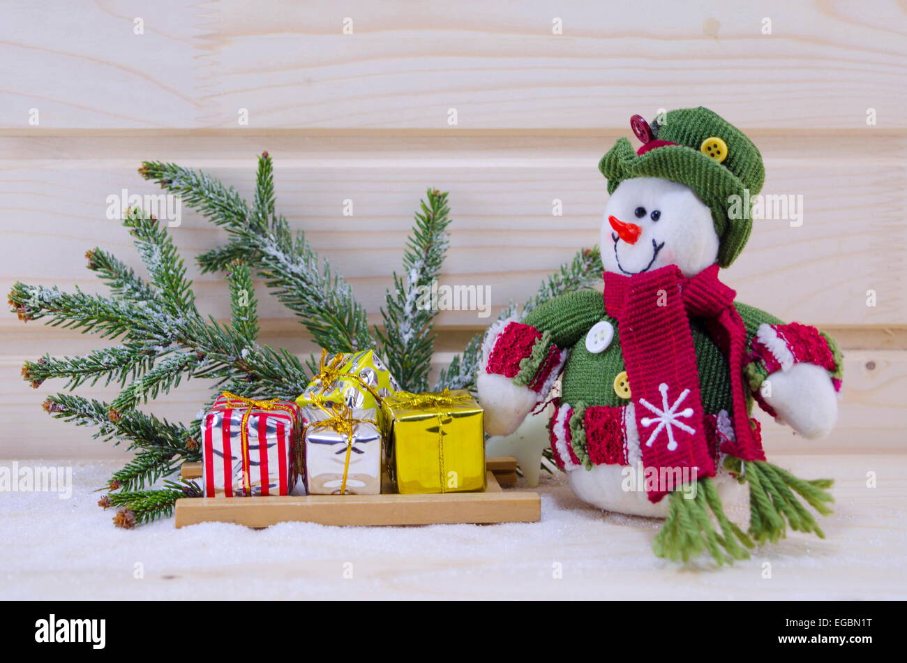 Toy Snowman among fir trees and presents on a snowy wooden surface Stock Photo