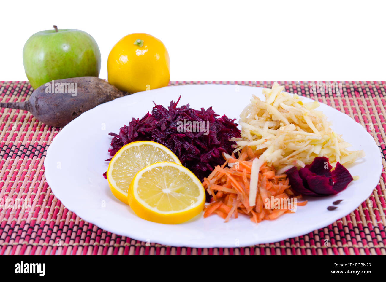 Grated carrots beet and apples with whole apples, lemon and bleet in the background Stock Photo