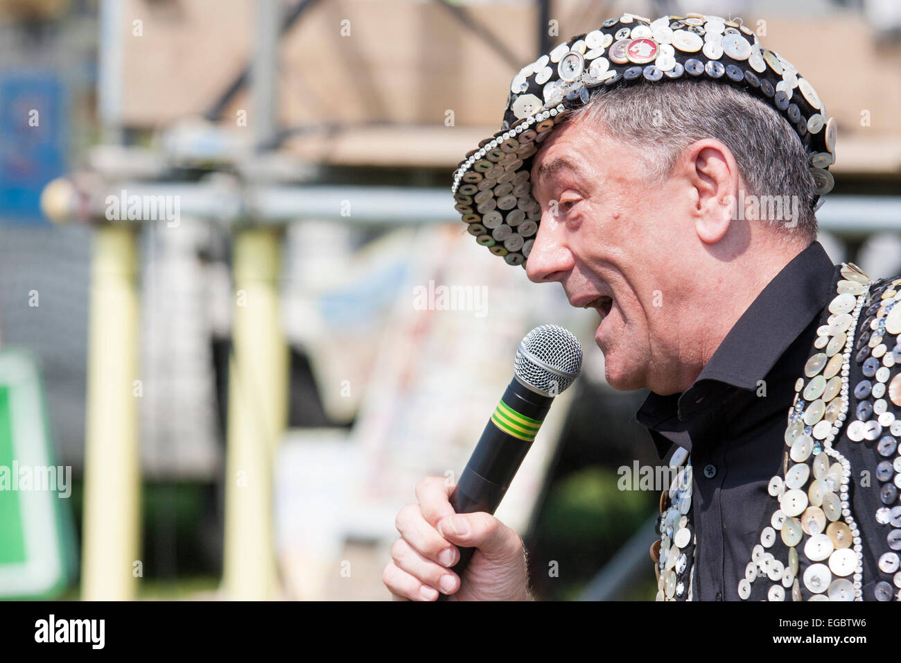 Mickie Driver, dressed in a pearly King waistcoat, jacket and hat, singing at an outdoor 1940s nostalgic event with hand held microphone. Stock Photo