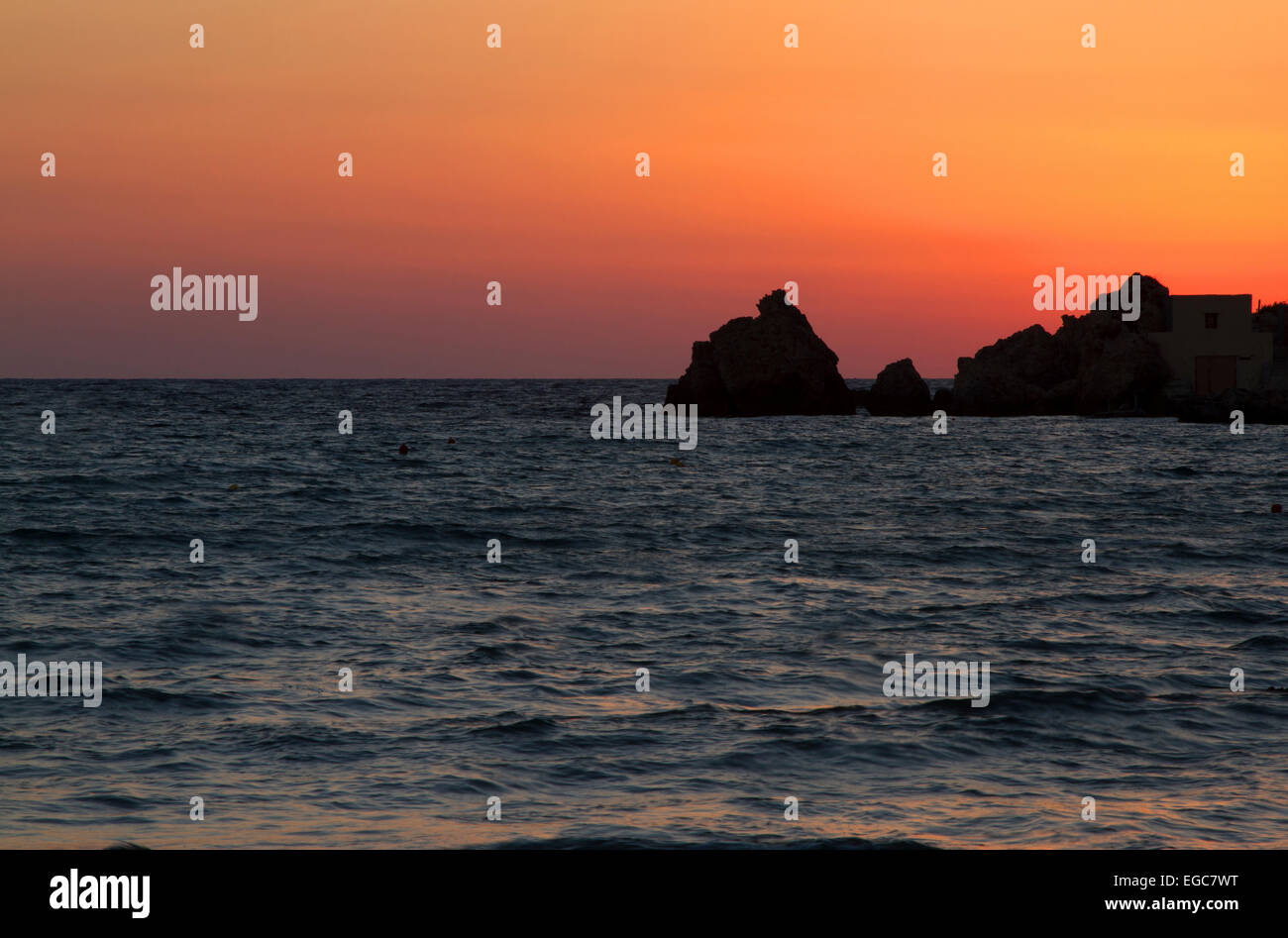 Setting sun behind rocks on the Malta coastline Stock Photo
