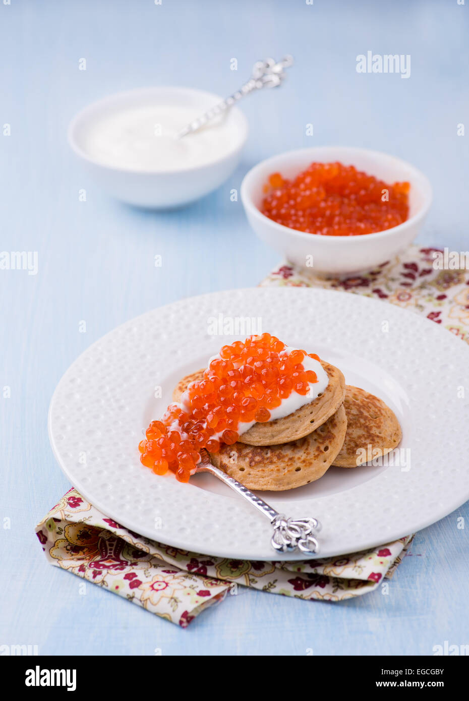 Buckwheat blini with red caviar and sour cream on white plate
