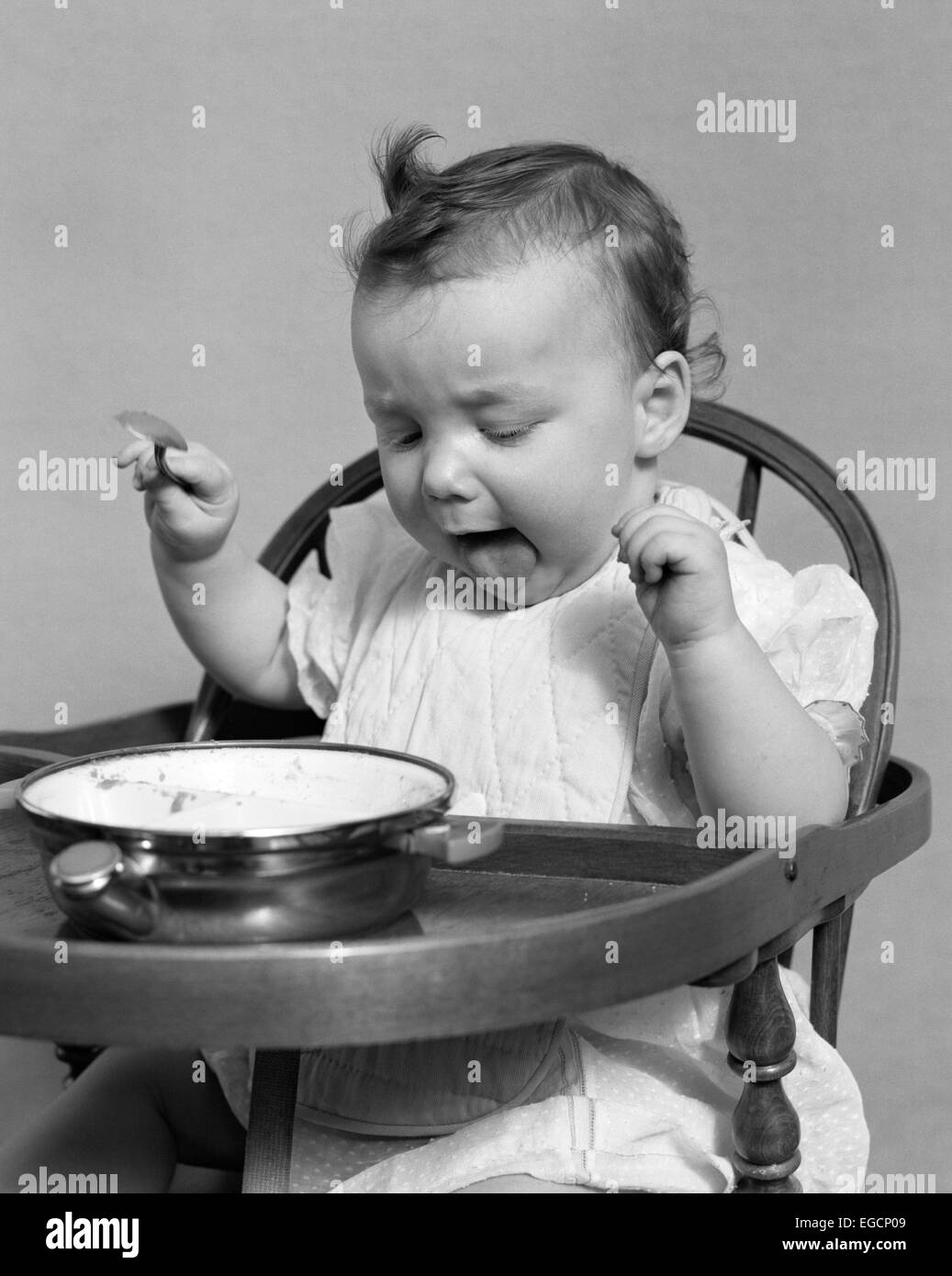 1940s BABY GIRL EATING FOOD IN HIGHCHAIR STICKING OUT TONGUE Stock Photo