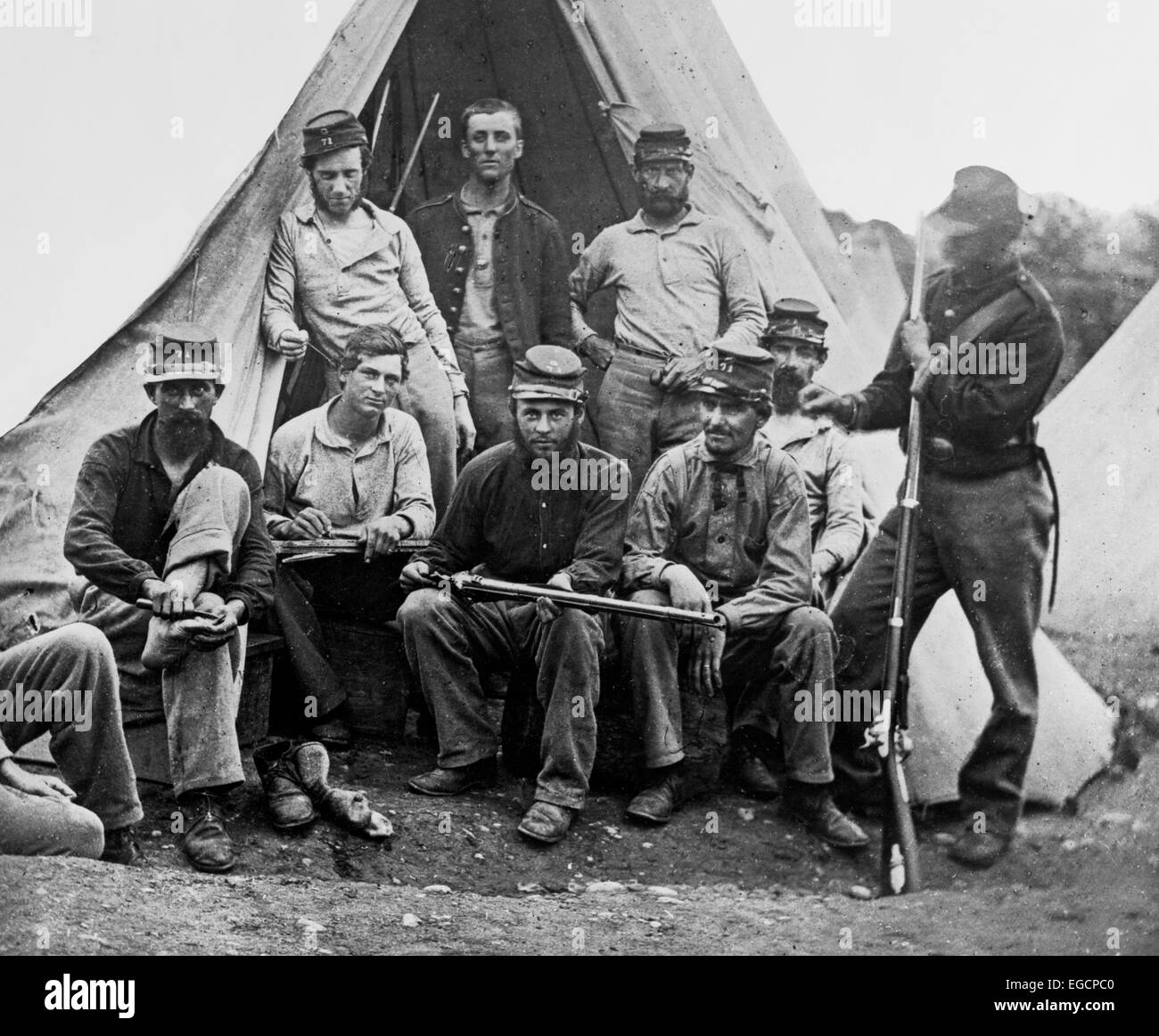 1860s GROUP OF NINE UNION SOLDIERS SEATED IN FRONT OF TENT HOLDING RIFLES LOOKING AT CAMERA Stock Photo