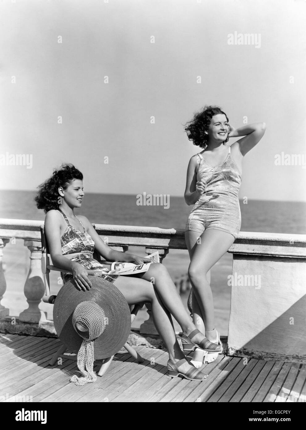 1930s 1940s TWO WOMEN SITTING ON HOTEL DECK BEACH SIDE IN ONE PIECE BATHING SUIT FASHION FLORIDA USA Stock Photo