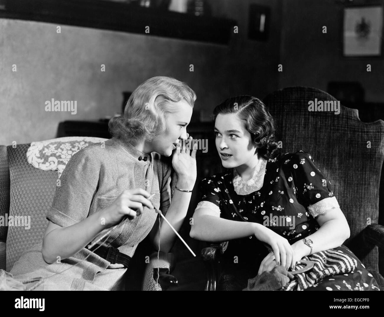 1930s TWO WOMEN SITTING IN CHAIRS IN PRIVATE CONVERSATION WOMAN HAS HAND TO SIDE OF MOUTH TO TELL SECRET Stock Photo