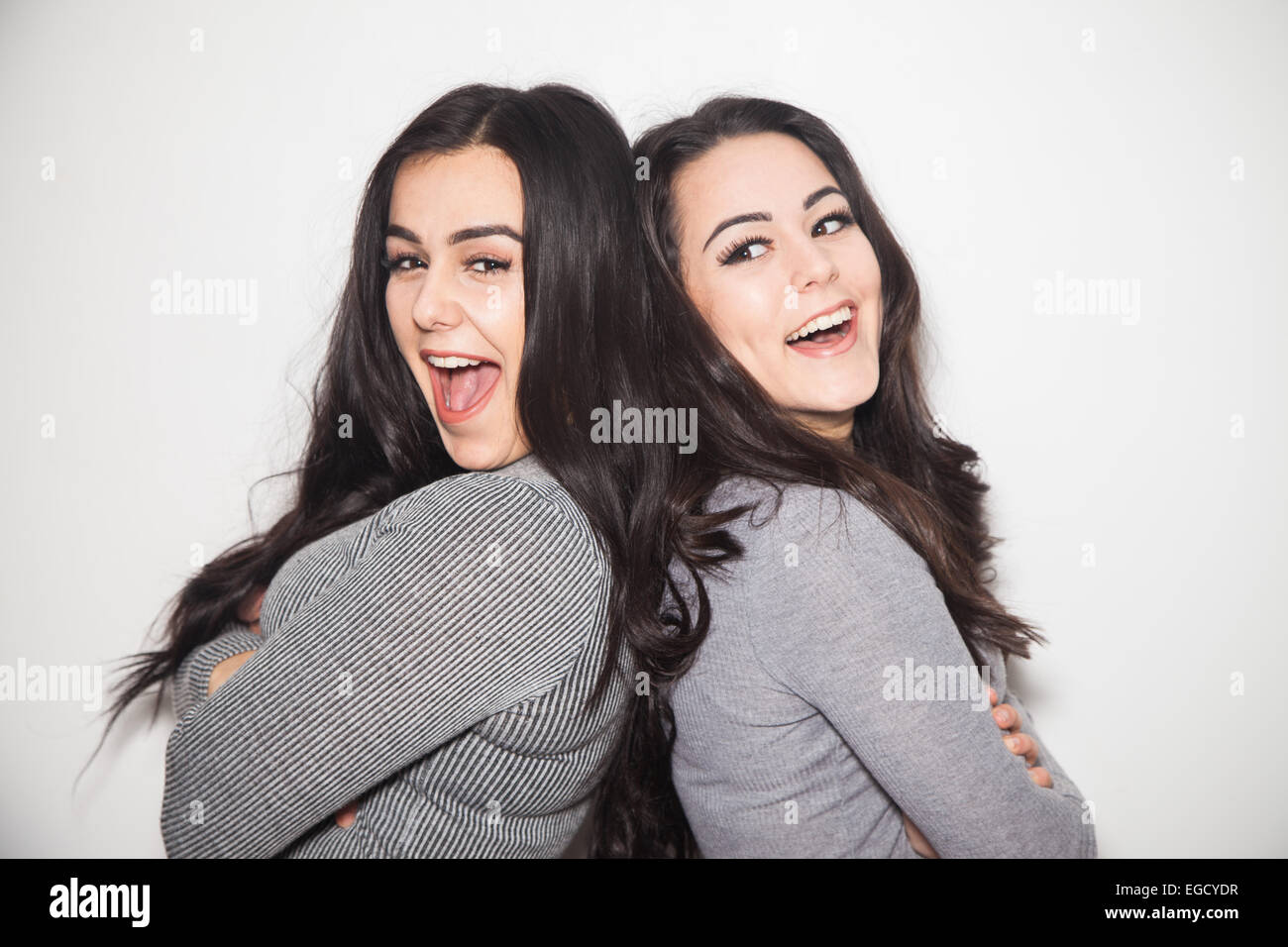 Two sisters leaning back to back laughing. Stock Photo